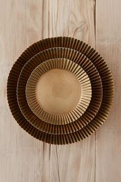 three gold plates sitting on top of a wooden table next to a knife and fork