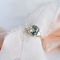 an engagement ring with a large green stone on top of white fabric and pink satin