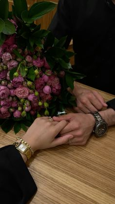 two people holding hands over a bouquet of flowers