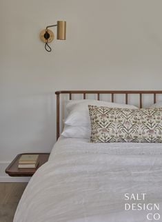 a bed with white sheets and pillows in a bedroom next to a wall mounted lamp