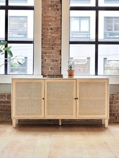 the sideboard is in front of two large windows and a potted plant on top