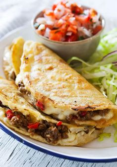 a white plate topped with two quesadillas next to a bowl of salad