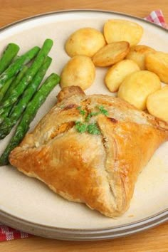 a white plate topped with meat and potatoes next to asparagus