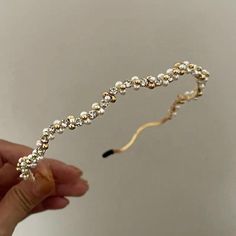 a hand holding a gold and white headband with pearls on it's side