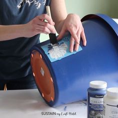 a woman is painting the inside of a blue barrel with flowers on it and glue