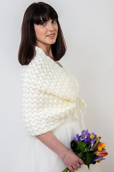 a woman in a white dress holding a bouquet of flowers and wearing a knitted shawl