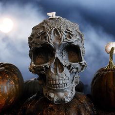 a skull statue sitting on top of pumpkins in front of a dark cloudy sky