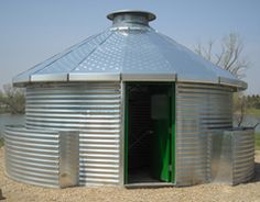 a round metal structure with a green door in the middle of dirt area next to water