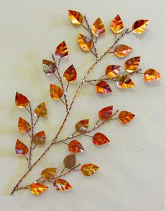 a metal branch with orange leaves on top of white surface next to a red and yellow vase