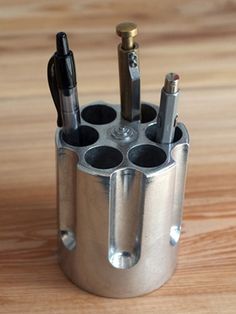 a metal cup holder with pens and pencils in it on a wooden table top