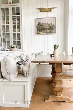 a cat sitting on top of a bench next to a wooden table in a living room