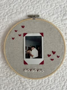 an embroidered photo frame with red hearts on it and two people kissing in the background