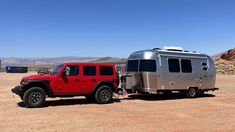 a red jeep towing a silver trailer in the desert