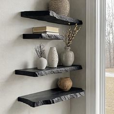 three black shelves with books and vases on them in front of a window sill