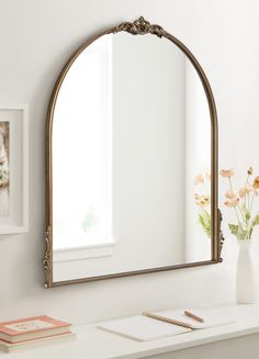 a mirror sitting on top of a white table next to a vase with flowers in it