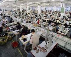 an industrial factory with lots of people working on sewing machines and desks in the foreground