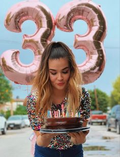 a woman holding a cake with candles on it in front of the number thirty three