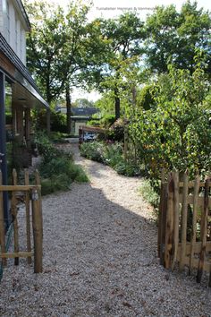 a gravel path between two buildings with trees in the background