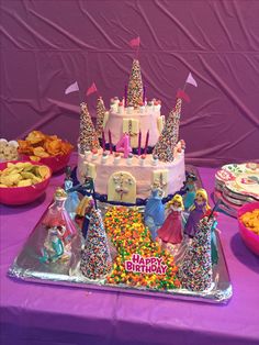 a birthday cake is decorated with princess figures and sprinkles on a purple tablecloth