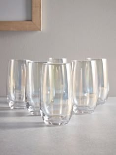 six clear wine glasses lined up on a white countertop next to a framed photograph