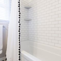 a white bath tub sitting under a window next to a towel rack and shower curtain