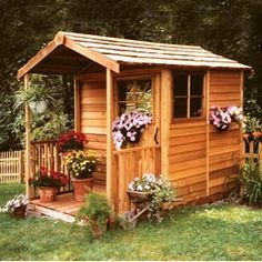 a small wooden garden shed with flowers in the window boxes on the front and side