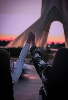 two people holding their hands up in front of the eiffel tower at sunset