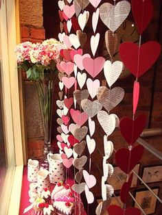 a bunch of hearts hanging from the side of a wall next to a vase with flowers in it