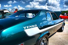 an old blue car parked in a parking lot next to other cars and people looking at it