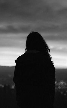 a person standing in front of a cityscape with the sky covered in clouds