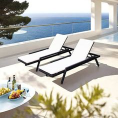 two chaise lounge chairs sitting on top of a patio next to an ocean view