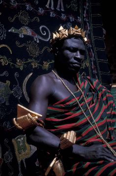 a man with a crown on his head sitting in front of a cloth covered wall