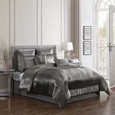 a bed with silver sheets and pillows in a room next to a door that leads to a patio