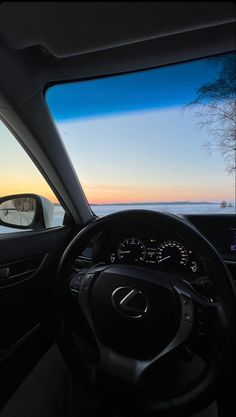 the inside view of a car driving on a road near water and trees at sunset