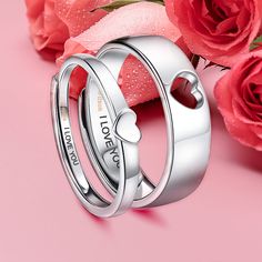 two silver rings with hearts on them sitting next to pink roses and one red rose