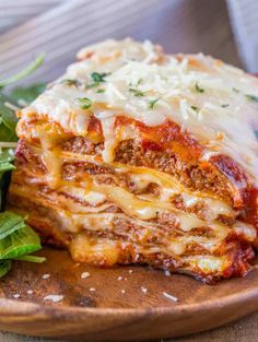 a wooden plate topped with lasagna covered in sauce and cheese next to a salad