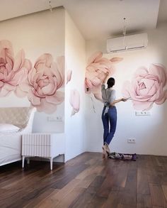 a woman painting flowers on the wall in a room with wood floors and white walls