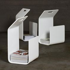 two white magazine racks with magazines in them on concrete floor next to cement wall,