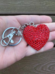 a hand holding a red heart shaped keychain with scissors on it's side