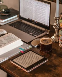 an open book sitting on top of a wooden desk next to a laptop and phone