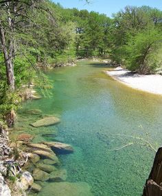 a river running through a forest filled with rocks and green trees on the side of it