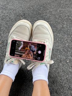 a person's feet wearing white tennis shoes while holding a cell phone