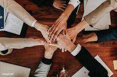 several people are holding hands in the middle of a table with papers and pens on it