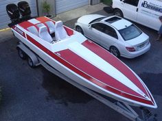 a red and white boat parked next to a car