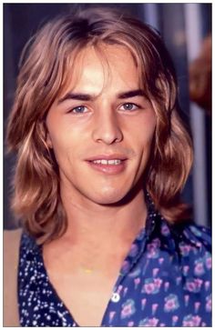 a man with long hair and blue eyes wearing a flowered shirt is looking at the camera