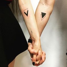 two people holding hands with small tattoos on their arms, one is black and the other is white