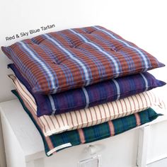 three pillows stacked on top of each other in front of a white wall with text reading red & sky blue tartan