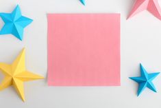 three paper stars next to a pink sheet of paper with blue and yellow origami stars