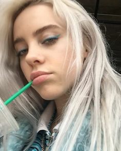 a woman with long white hair and blue eyes is holding a green straw in her mouth