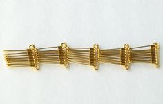 four pieces of gold colored hair pins on a white surface with clippings attached to them